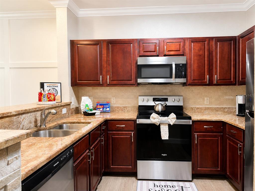 A kitchen features dark wood cabinets, granite countertops, stainless steel appliances, and a double sink — 1301 TUSCAN TERRACE UNIT 9205, DAVENPORT, FL