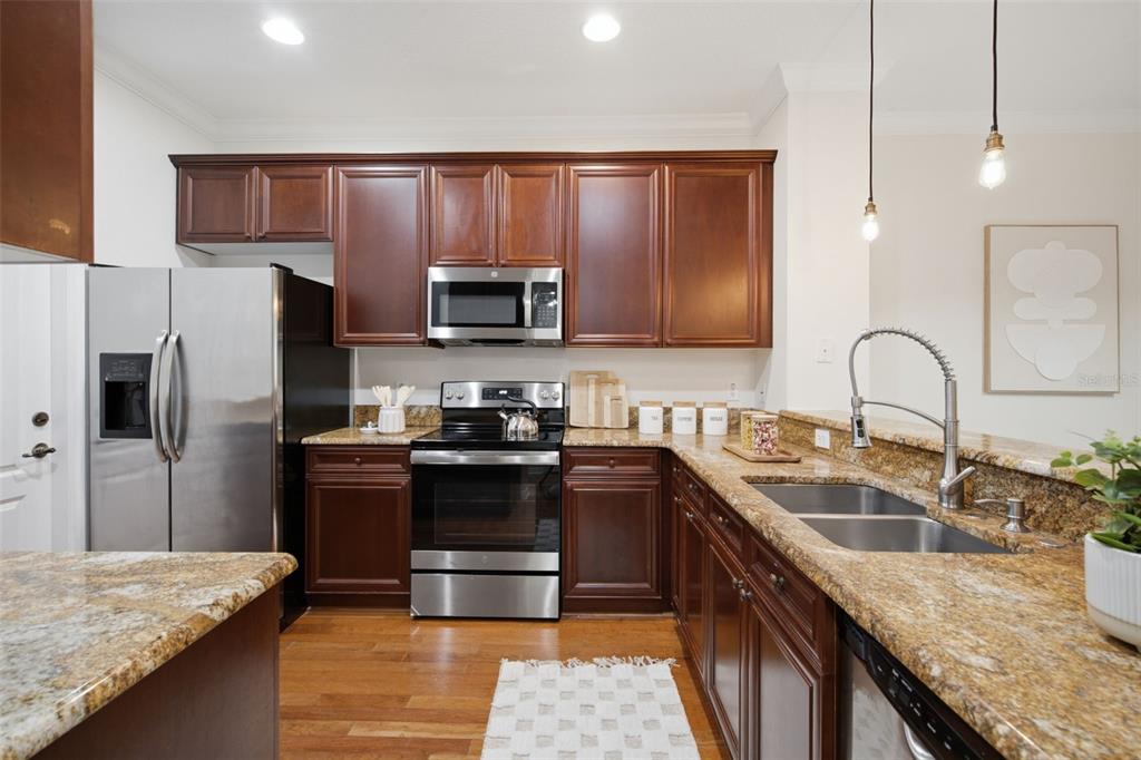 A kitchen features dark wood cabinets, granite countertops, stainless steel appliances, and hardwood flooring — 5957 STRADA CAPRI WAY, ORLANDO, FL