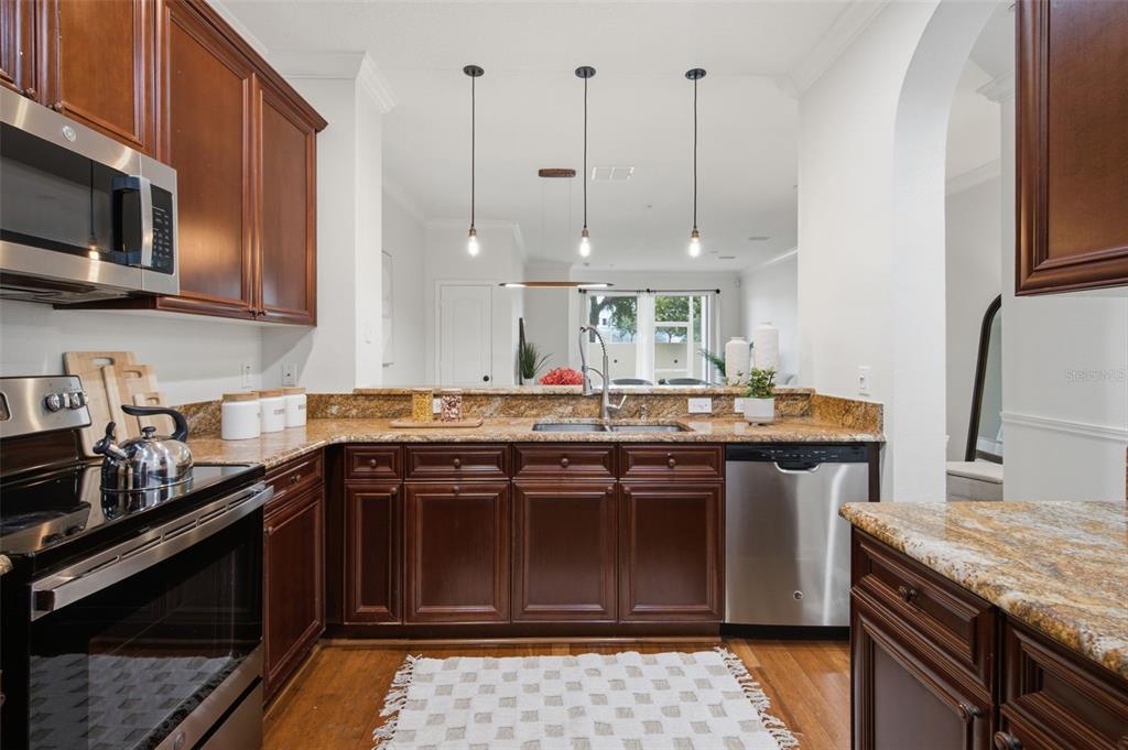 A kitchen features dark wood cabinets, granite countertops, stainless steel appliances, and hardwood floors — 5957 STRADA CAPRI WAY, ORLANDO, FL