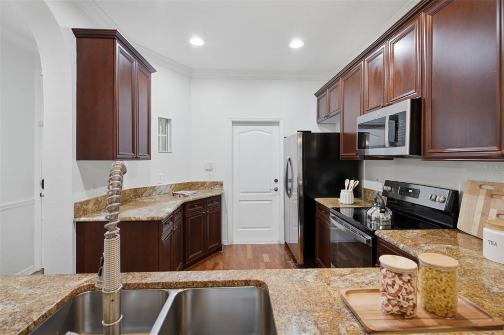 A kitchen with dark wood cabinets, granite countertops, stainless steel appliances, and a double sink — 5957 STRADA CAPRI WAY, ORLANDO, FL