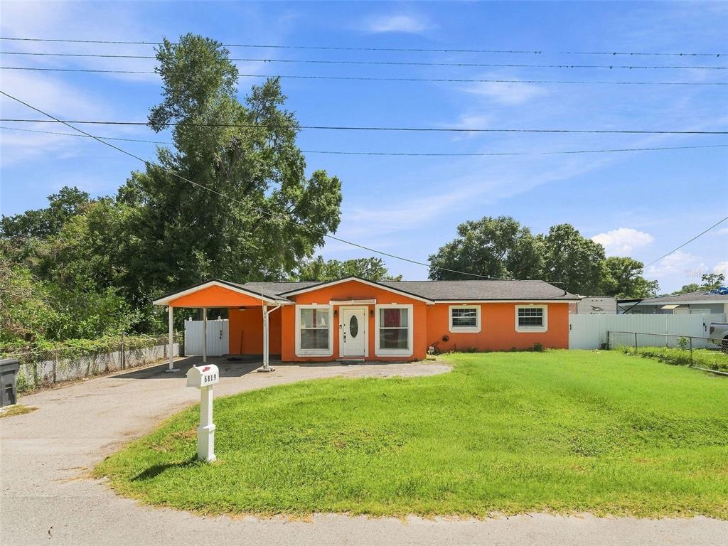 A single-story orange house with a carport and a front lawn under a blue sky — 6819 32ND AVENUE S, TAMPA, FL