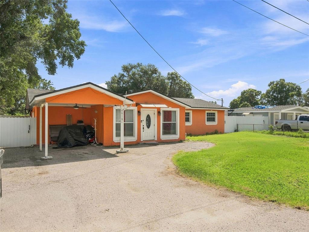 A single-story orange house with a carport and a gravel driveway under a blue sky — 6819 32ND AVENUE S, TAMPA, FL