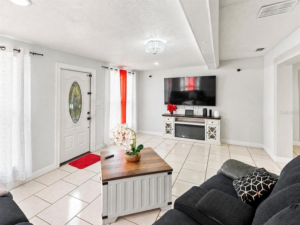 A living room features white tile floors, a wall-mounted television, and a white media console — 6819 32ND AVENUE S, TAMPA, FL
