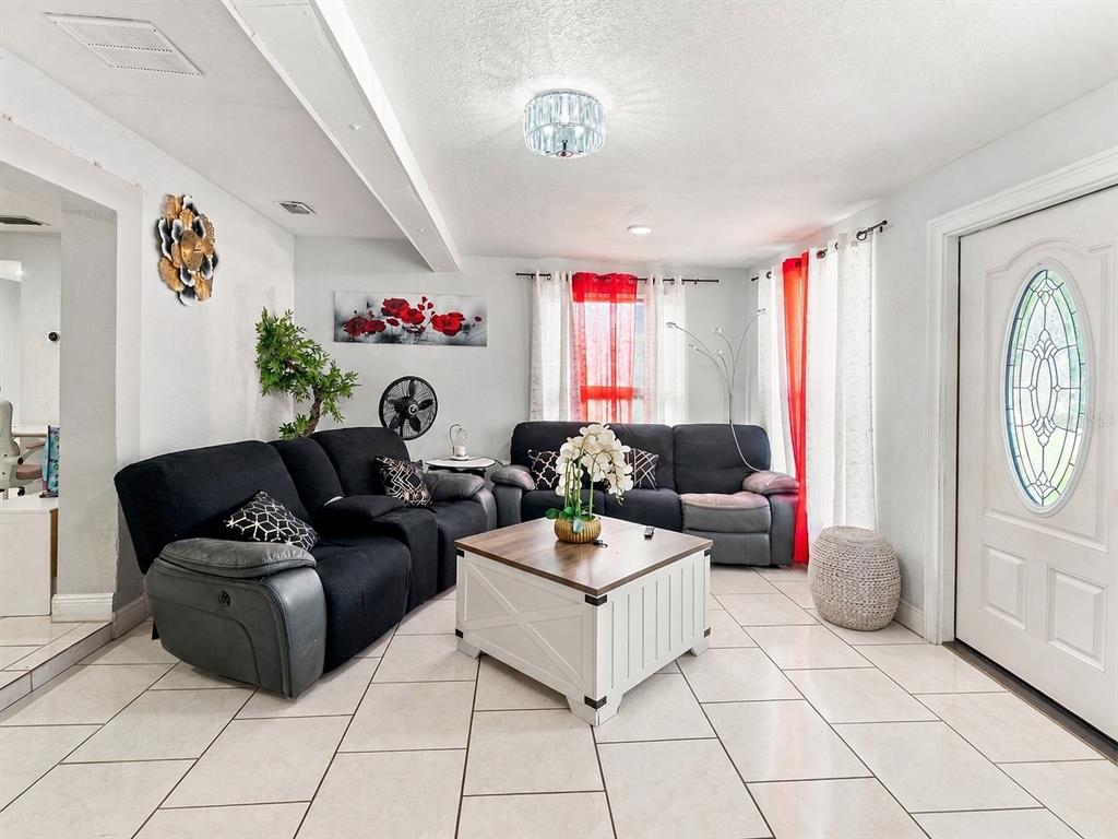 A living room features black reclining sofas, a white coffee table, and tile flooring — 6819 32ND AVENUE S, TAMPA, FL