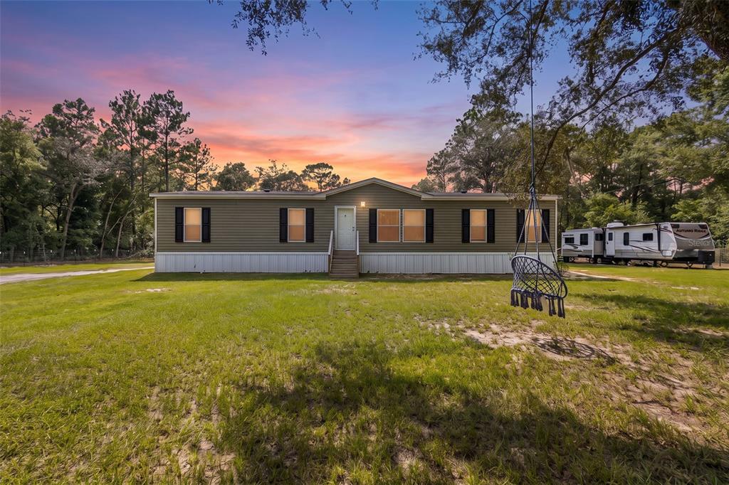 A single-story manufactured home with olive siding sits on a grassy lot at sunset — 7650 NE 105TH AVENUE, BRONSON, FL