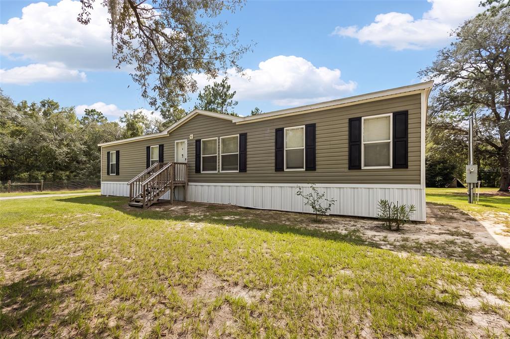 A single-story manufactured home with olive green siding, black shutters, and a wooden entrance staircase — 7650 NE 105TH AVENUE, BRONSON, FL