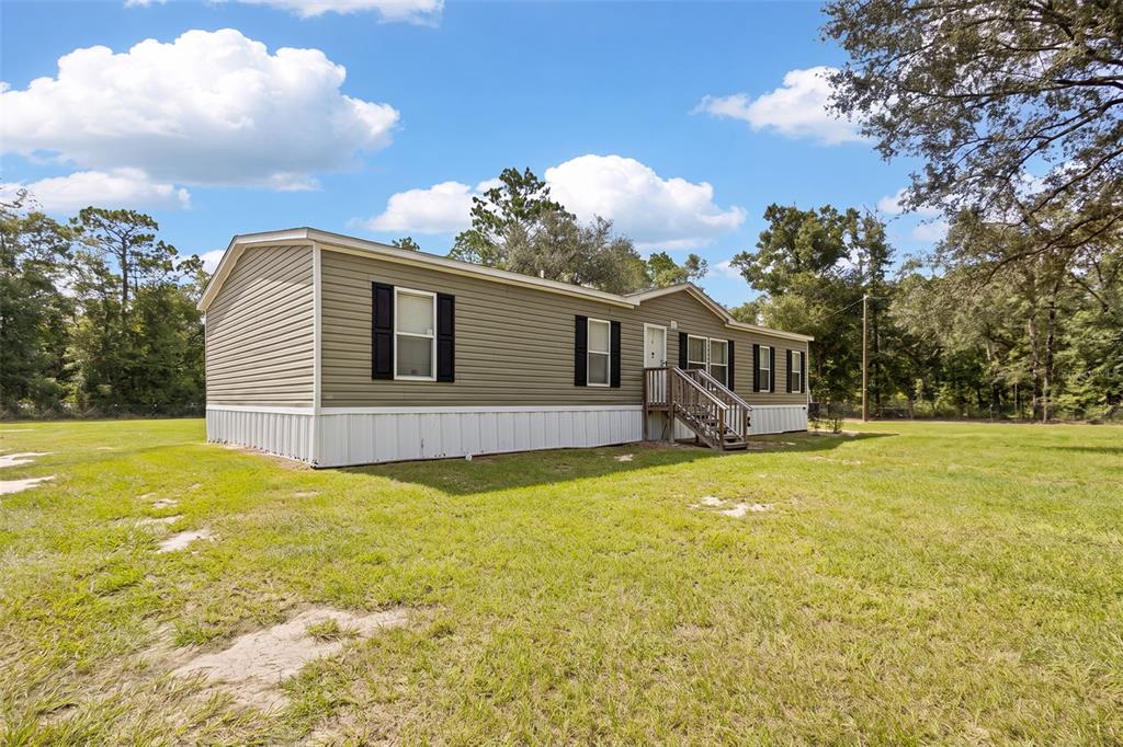 A single-story manufactured home with olive-green siding sits on a large, grassy lot — 7650 NE 105TH AVENUE, BRONSON, FL