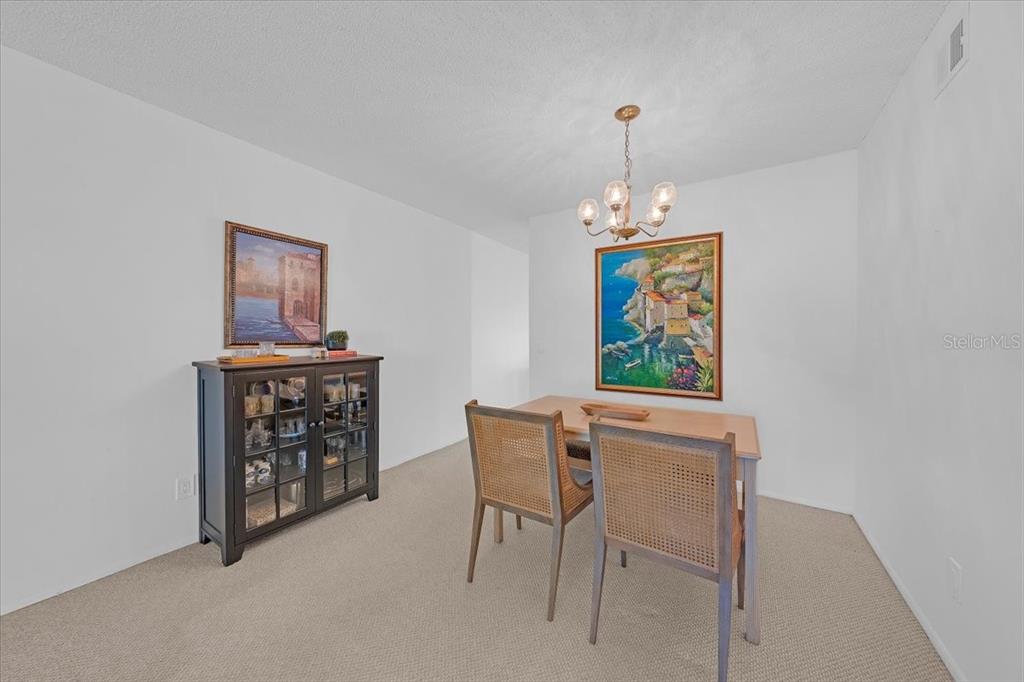 A dining room features a wooden table, two cane-back chairs, a dark cabinet, and artwork — 2401 FRANCISCAN DRIVE UNIT 41, CLEARWATER, FL