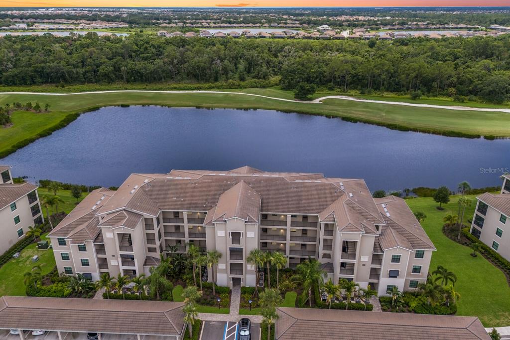 An aerial view of a multi-story apartment building situated next to a large pond — 17626 GAWTHROP DRIVE UNIT 106, BRADENTON, FL