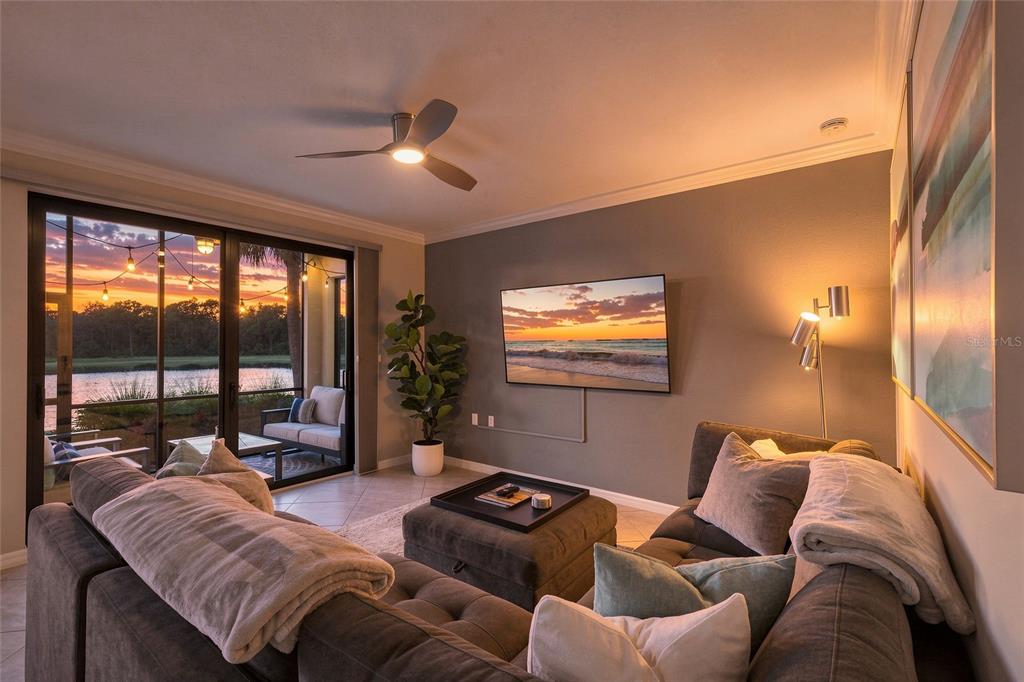 A living room with a sectional sofa, television, ceiling fan, and sliding doors to a patio — 17626 GAWTHROP DRIVE UNIT 106, BRADENTON, FL