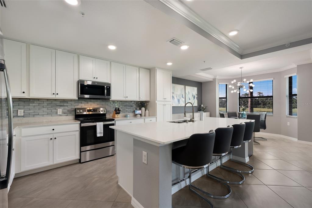 A modern kitchen features white cabinetry, a large island with bar seating, and stainless appliances — 17626 GAWTHROP DRIVE UNIT 106, BRADENTON, FL
