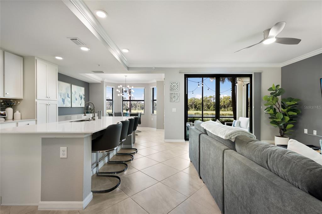 A modern open-concept kitchen and living area with a breakfast bar, tile floors, and patio — 17626 GAWTHROP DRIVE UNIT 106, BRADENTON, FL