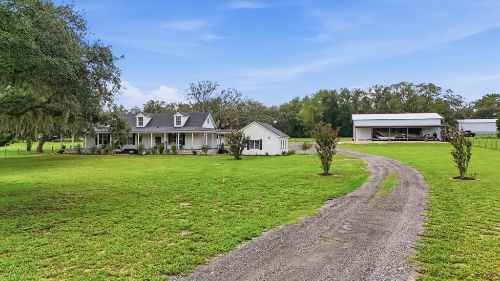 A white farmhouse with a porch and a detached garage sits on a grassy lot — 1750 W MANSFIELD STREET, LECANTO, FL