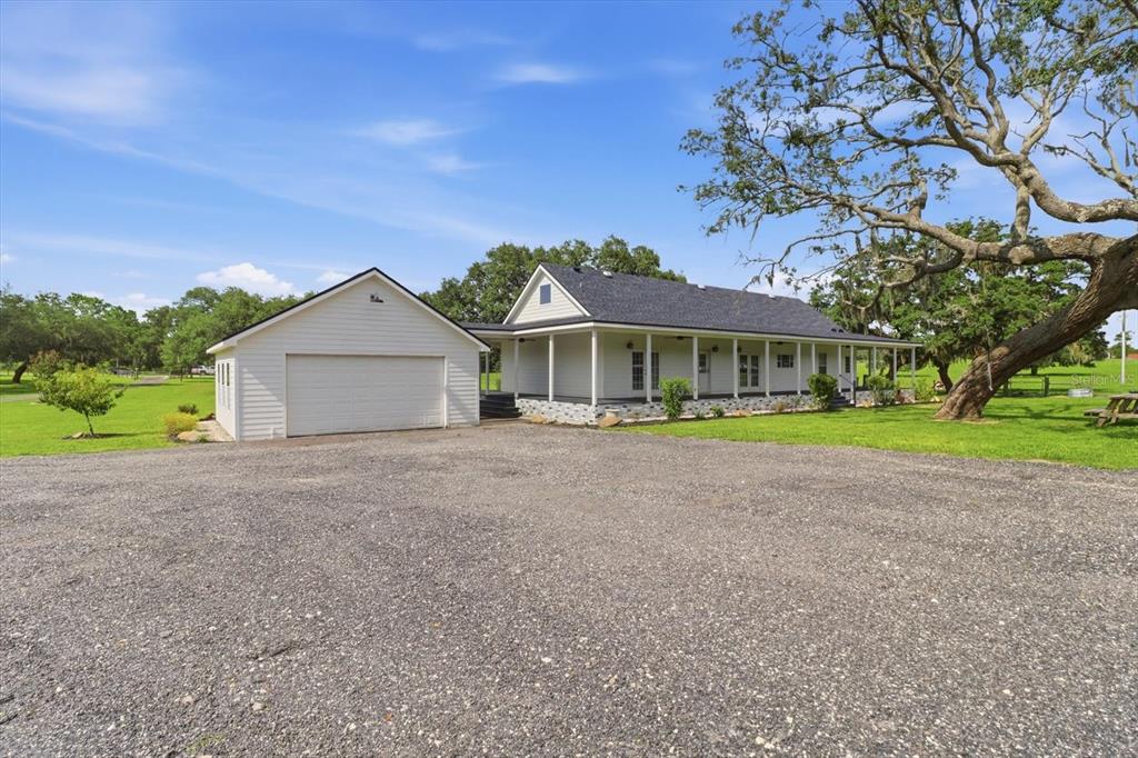 A white house with a detached garage and a large porch sits on a gravel lot — 1750 W MANSFIELD STREET, LECANTO, FL