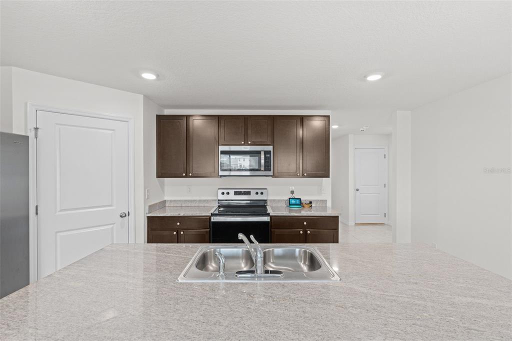 A kitchen with dark wood cabinets, granite countertops, a central island, and stainless steel appliances — 12210 KINGSLEY TRAIL, PARRISH, FL