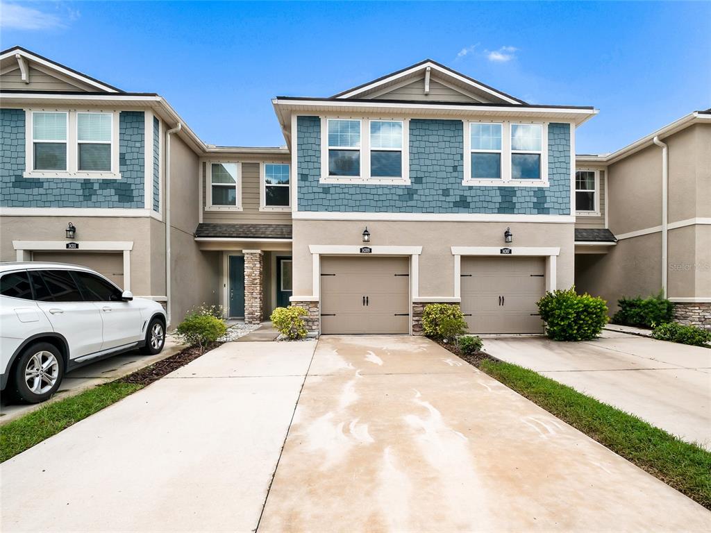 A two-story townhouse exterior features tan stucco, blue shingle siding, and two attached garages — 14309 PONDHAWK LANE, TAMPA, FL