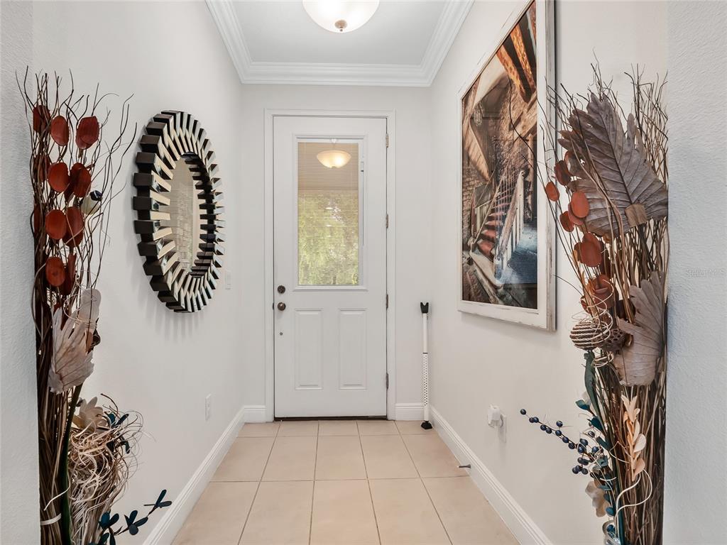 A tiled entryway features a white front door, a circular mirror, and two large floral arrangements — 14309 PONDHAWK LANE, TAMPA, FL