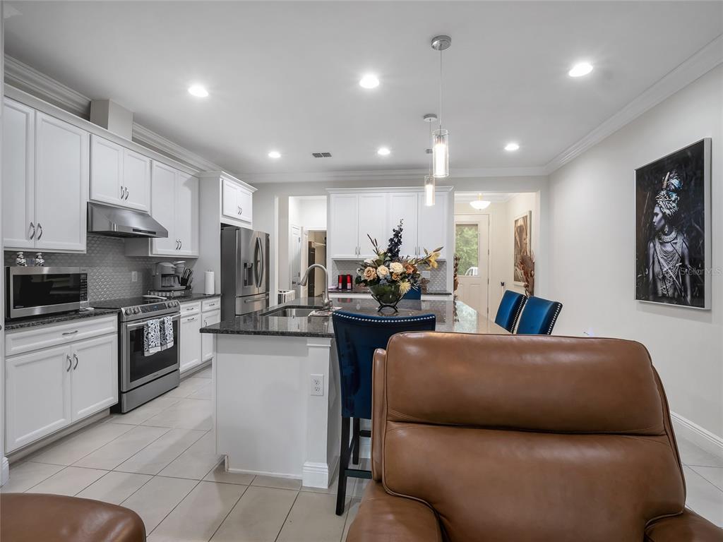 A modern kitchen features white cabinetry, granite countertops, a central island, and blue bar stools — 14309 PONDHAWK LANE, TAMPA, FL