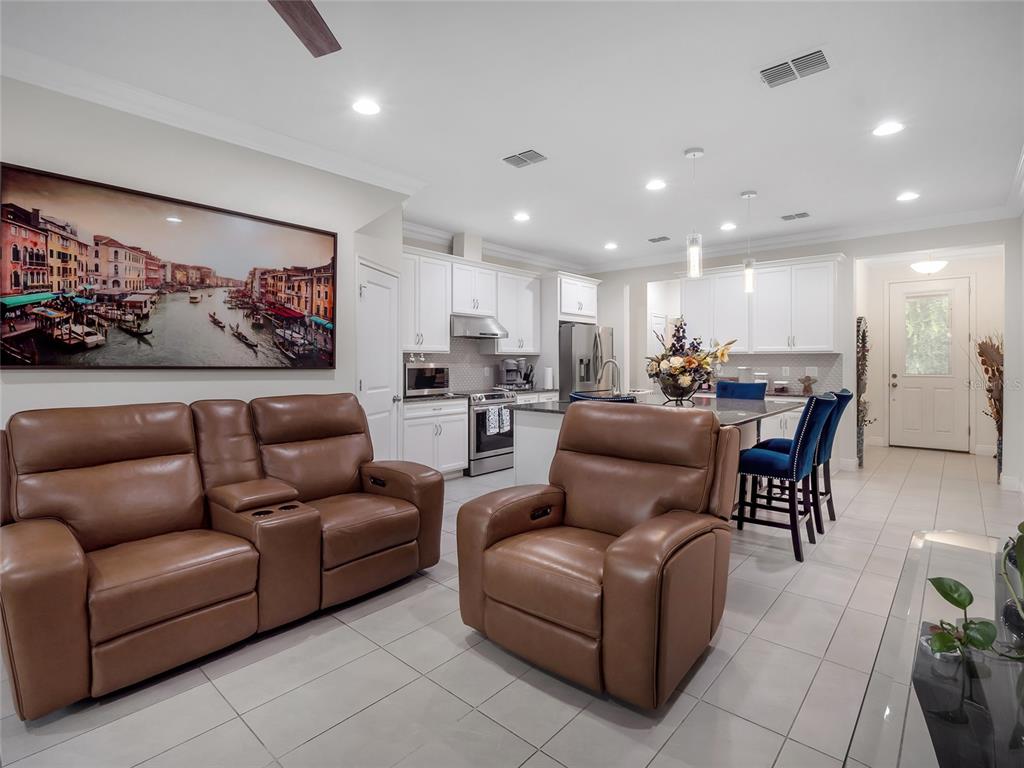 An open-concept living area features brown leather seating, a kitchen with white cabinets, and tile flooring — 14309 PONDHAWK LANE, TAMPA, FL