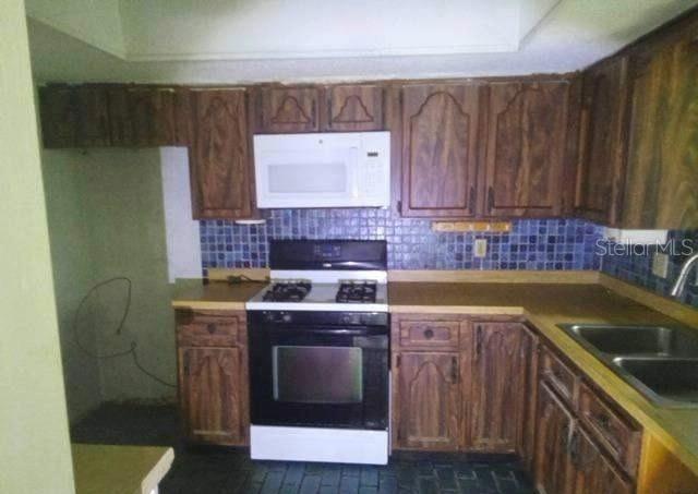 A kitchen features wood cabinets, a white microwave, a black stove, and blue tiled backsplashes — 3339 E WITHLACOOCHEE TRAIL, DUNNELLON, FL