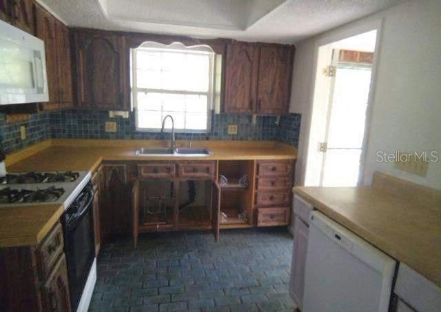 A kitchen features wood cabinets, a white microwave, a gas stove, and blue tile backsplash — 3339 E WITHLACOOCHEE TRAIL, DUNNELLON, FL