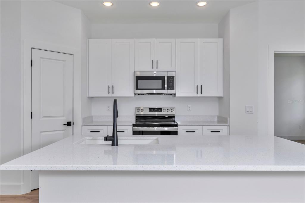 A modern kitchen features white cabinets, a quartz island with a black faucet, and stainless appliances — 78 FAIRWAY CIRCLE, UMATILLA, FL