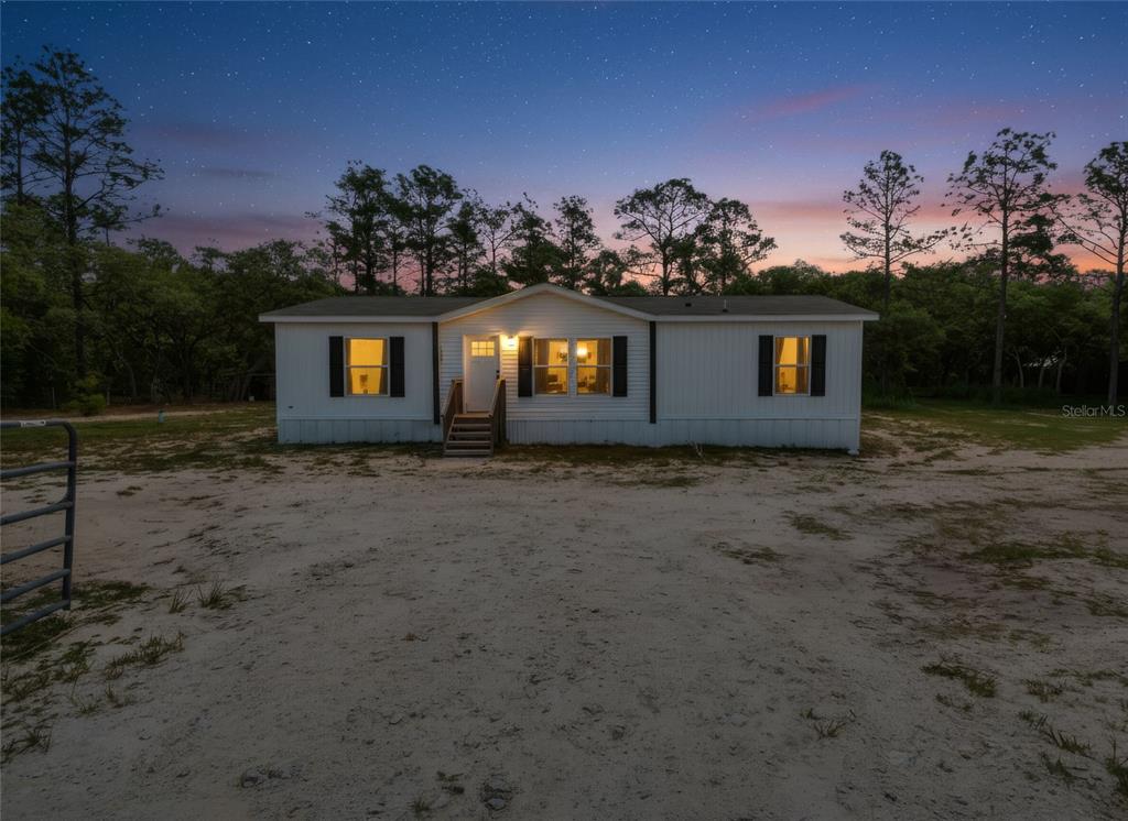 A white single-wide mobile home sits on a sandy lot at dusk — 5021 S ADVENTURE POINT, HOMOSASSA SPRINGS, FL