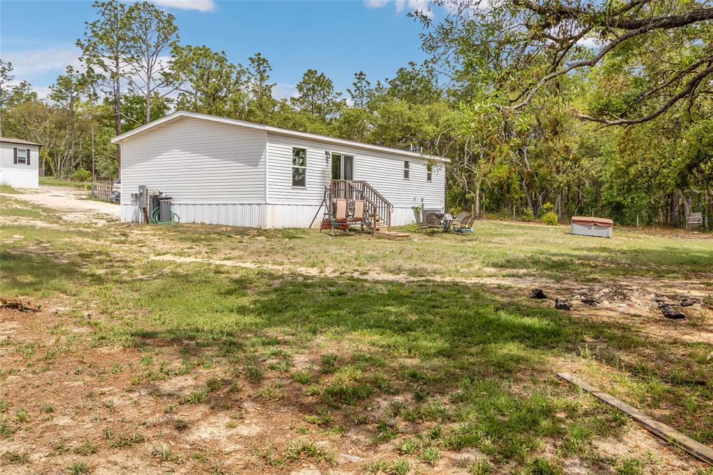 A white manufactured home sits on a grassy lot with a wooden deck and trees — 5021 S ADVENTURE POINT, HOMOSASSA SPRINGS, FL