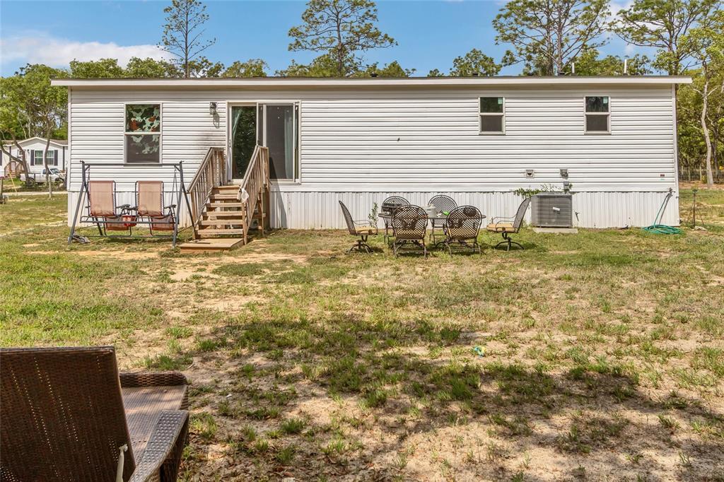 The exterior of a single-wide mobile home features white siding, a wooden staircase, and patio furniture — 5021 S ADVENTURE POINT, HOMOSASSA SPRINGS, FL