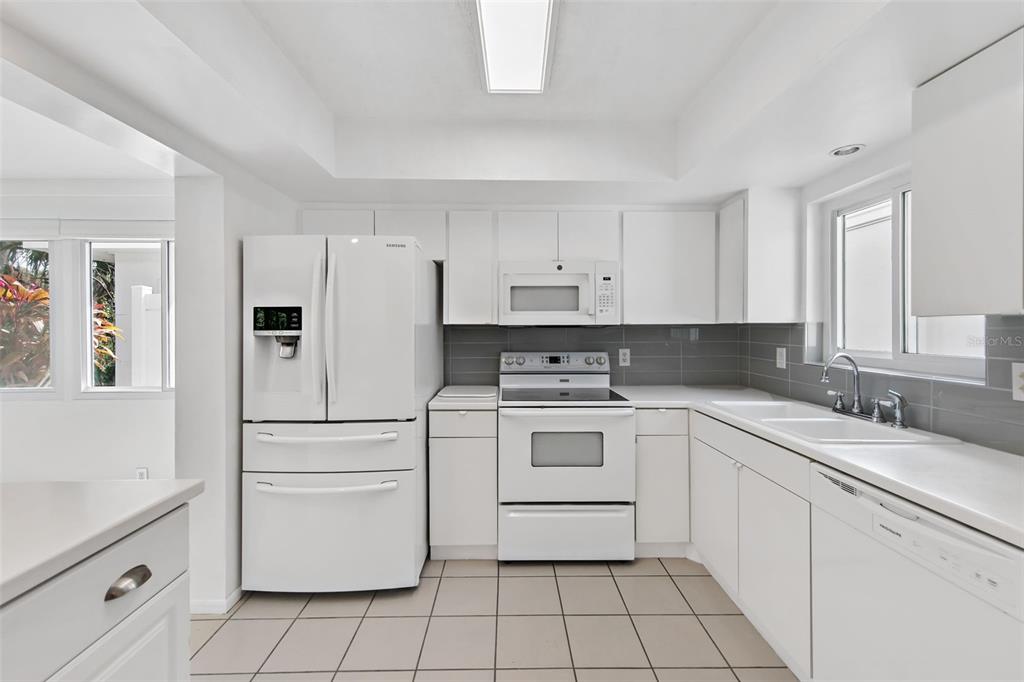A white kitchen features a refrigerator, stove, microwave, dishwasher, and grey tiled backsplash — 3915 SCHWALBE DRIVE UNIT 128, SARASOTA, FL