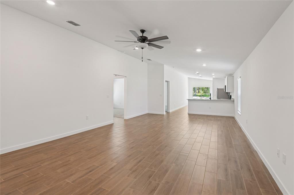 An open-concept living area features wood-look tile flooring, white walls, and a kitchen in back — 14133 CANADA GOOSE ROAD, WEEKI WACHEE, FL