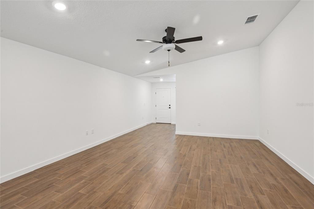 An empty room features white walls, a vaulted ceiling with a fan, and wood-look flooring — 14133 CANADA GOOSE ROAD, WEEKI WACHEE, FL