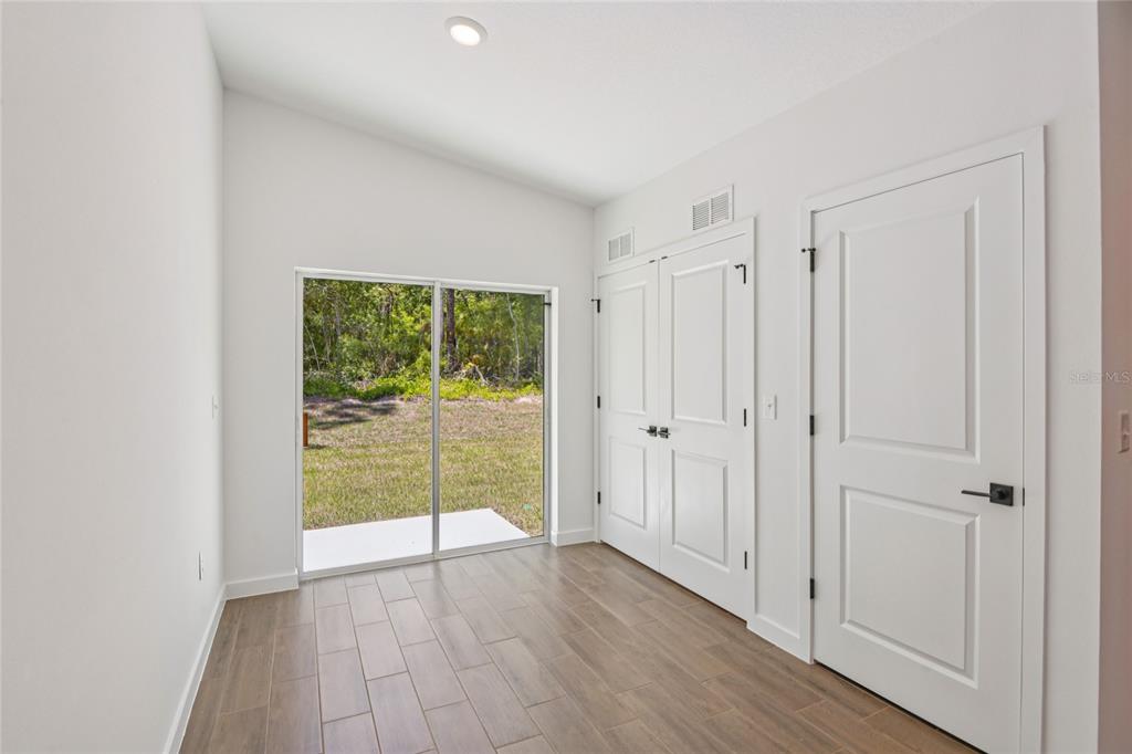 A room with white walls, wood-look tile flooring, a sliding glass door, and two doors — 14133 CANADA GOOSE ROAD, WEEKI WACHEE, FL