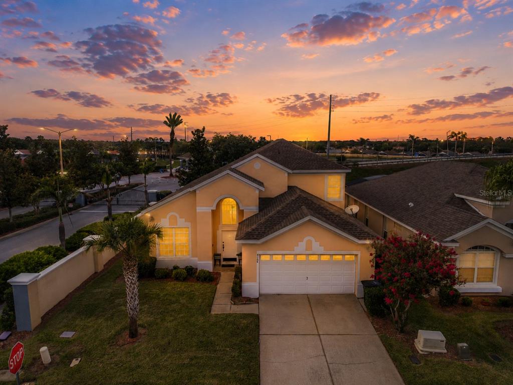An aerial view of a yellow suburban house with a two-car garage at sunset — 8184 FAN PALM WAY, KISSIMMEE, FL