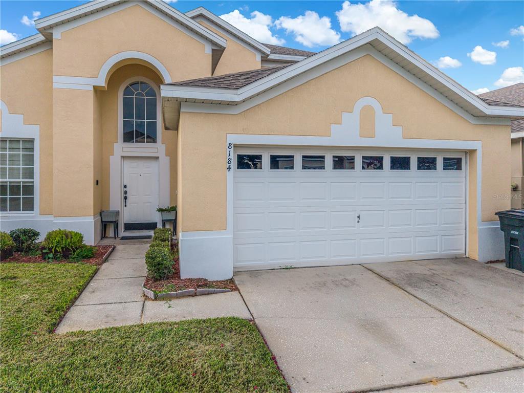 A beige two-story house features a white garage door and an arched entryway — 8184 FAN PALM WAY, KISSIMMEE, FL