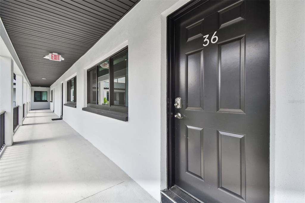 A black door marked 36 opens onto a white exterior walkway with an exit sign — 2942 W BAY DRIVE UNIT 16, BELLEAIR BLUFFS, FL