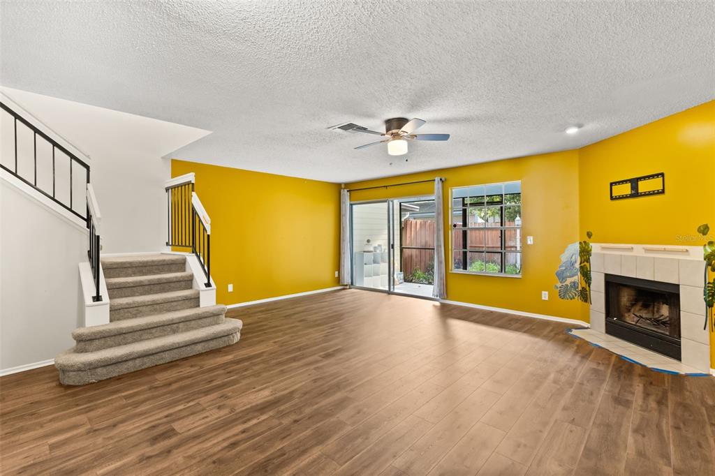 A living room with yellow walls, wood-look flooring, a fireplace, and stairs with carpeted steps — 2776 LANCASTER COURT, APOPKA, FL
