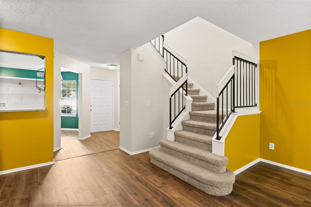 An entryway features a carpeted staircase with black railings, wood-look flooring, and bright yellow walls — 2776 LANCASTER COURT, APOPKA, FL