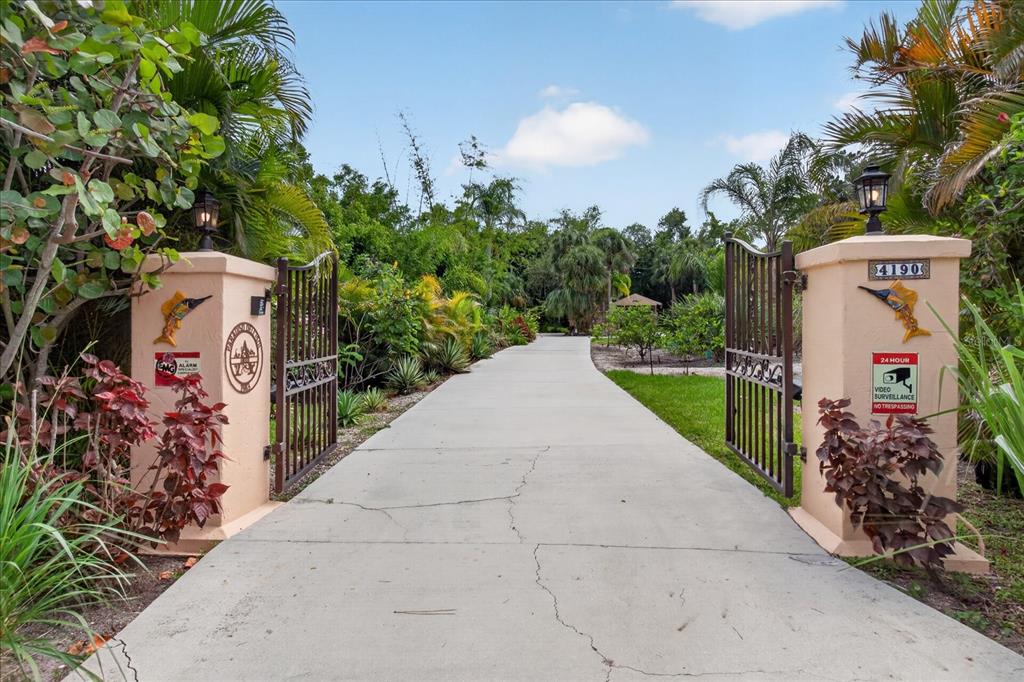 A concrete driveway leads through an open metal gate between two stucco pillars with lanterns — 4190 STROMBUS ROAD, VENICE, FL