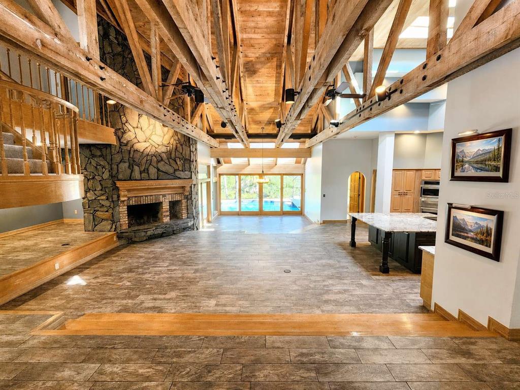 A spacious living area features exposed wooden trusses, a stone fireplace, and tile flooring — 3522 SHORELINE CIRCLE, PALM HARBOR, FL