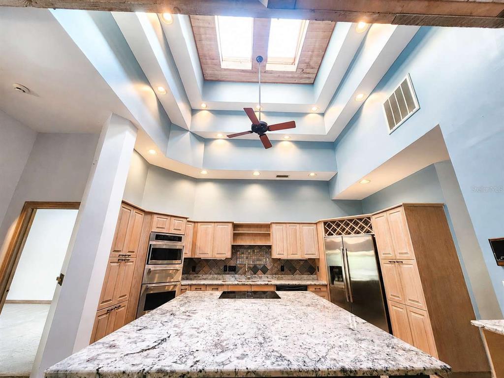 A kitchen features light wood cabinets, a large granite island, and a tiered skylight ceiling — 3522 SHORELINE CIRCLE, PALM HARBOR, FL