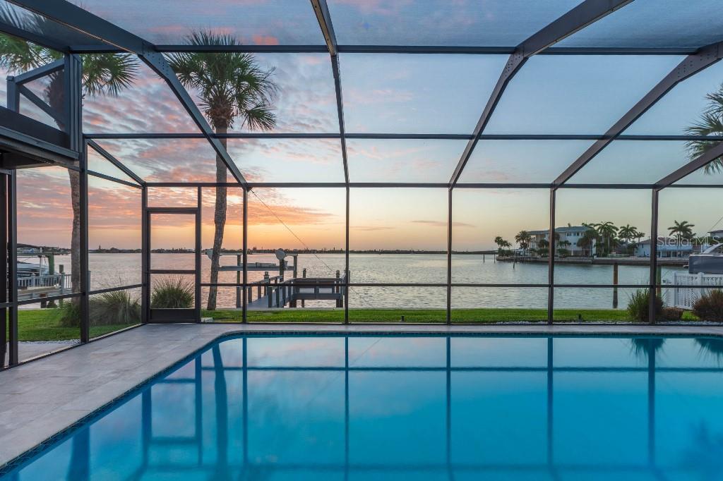A swimming pool sits inside a screened-in lanai overlooking a waterfront view at sunset — 306 BUTTONWOOD LANE, LARGO, FL