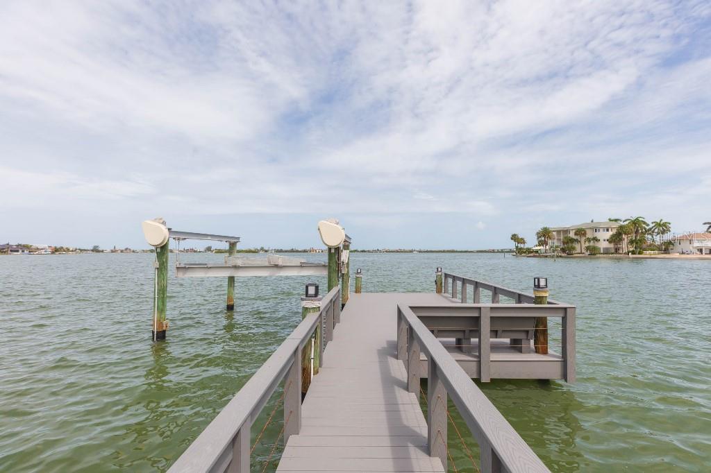 A wooden dock with a boat lift extends over the water toward a distant shoreline — 306 BUTTONWOOD LANE, LARGO, FL