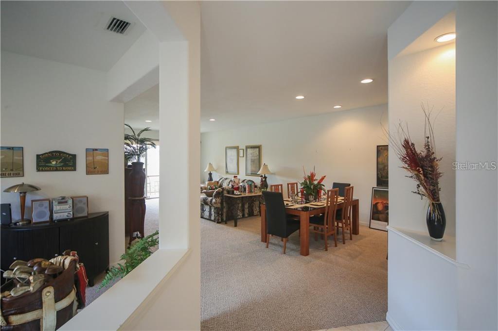 An open-concept living and dining area features carpeted floors, recessed lighting, and neutral wall paint — 8218 EAGLE ISLES PLACE, BRADENTON, FL