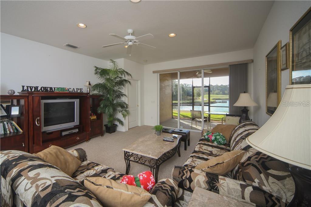 A living room features patterned sofas, a stone-topped coffee table, and sliding doors to a patio — 8218 EAGLE ISLES PLACE, BRADENTON, FL