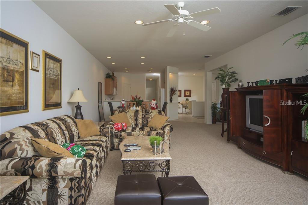 A living room features patterned sofas, a stone-topped coffee table, and a large entertainment center — 8218 EAGLE ISLES PLACE, BRADENTON, FL