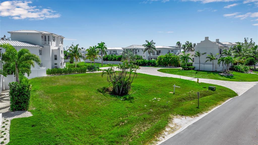 A grassy vacant lot sits between white multi-story houses under a clear blue sky — 610 HIBISCUS WAY, LONGBOAT KEY, FL