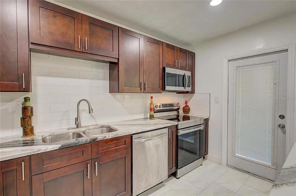 A kitchen with dark wood cabinets, stainless steel appliances, and white subway tile backsplash — 1008 CHESTER DRIVE, CLEARWATER, FL