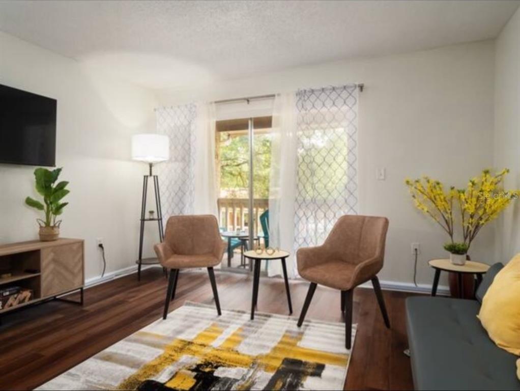 A living room features wood-look flooring, two tan chairs, a patterned rug, and sliding glass doors — 1810 NW 23RD BOULEVARD UNIT 178, GAINESVILLE, FL