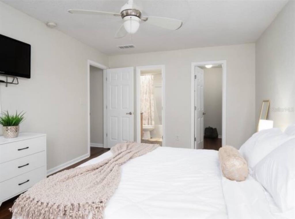 A bedroom features a white bed, a dresser with a plant, and three doorways — 1810 NW 23RD BOULEVARD UNIT 178, GAINESVILLE, FL